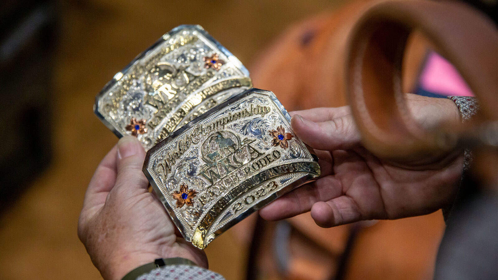 hands holding two trophy buckles from the 2023 WRCA World Championship Ranch Rodeo